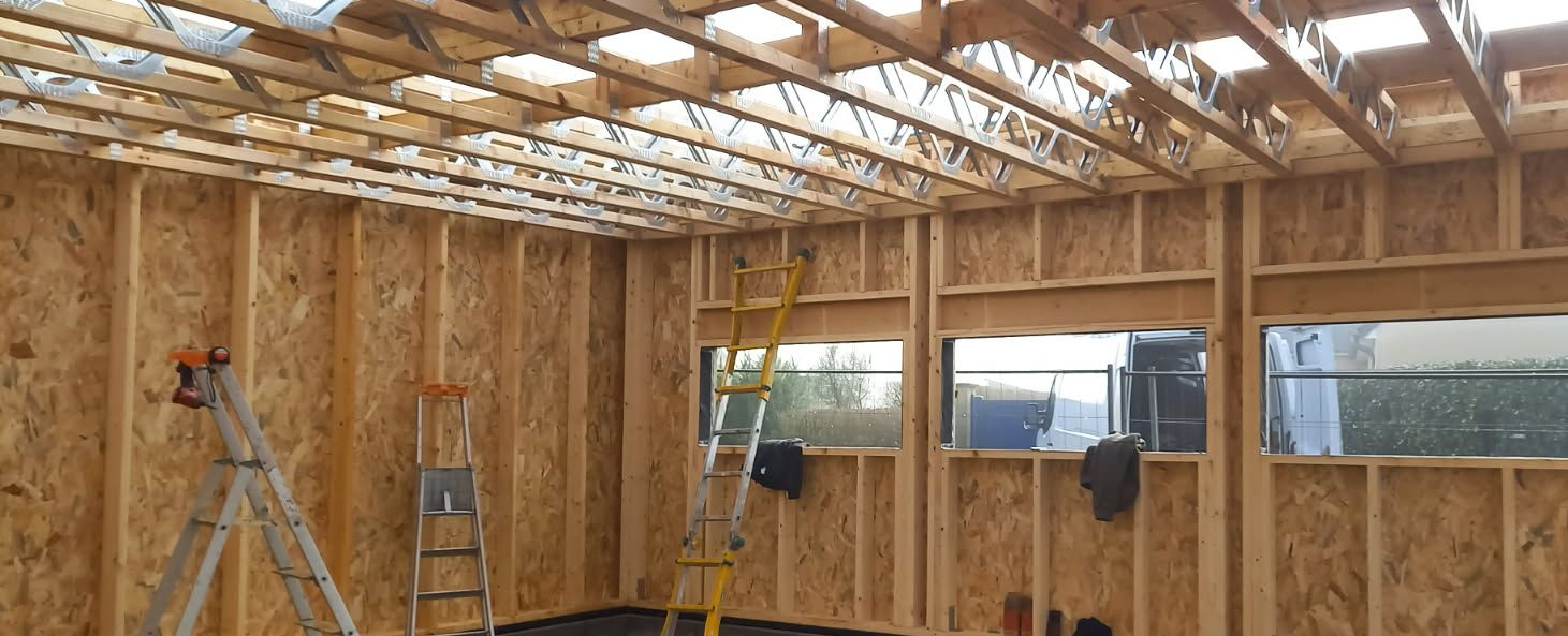 Intérieur d'un bâtiment en construction avec ossature en bois apparente, murs en OSB et chevrons visibles.