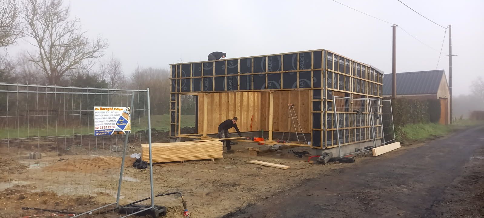 Construction d'une structure en bois sur un terrain boueux ; une personne travaille à l'intérieur.