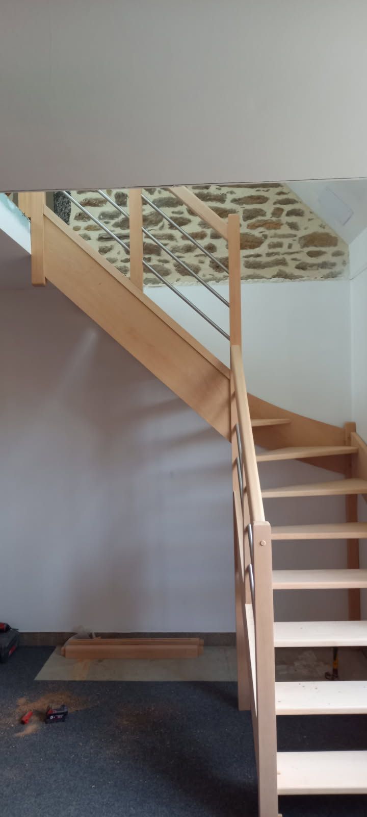 Escalier en bois avec une finition de couleur claire, menant vers le haut contre un mur blanc et un plafond texturé.