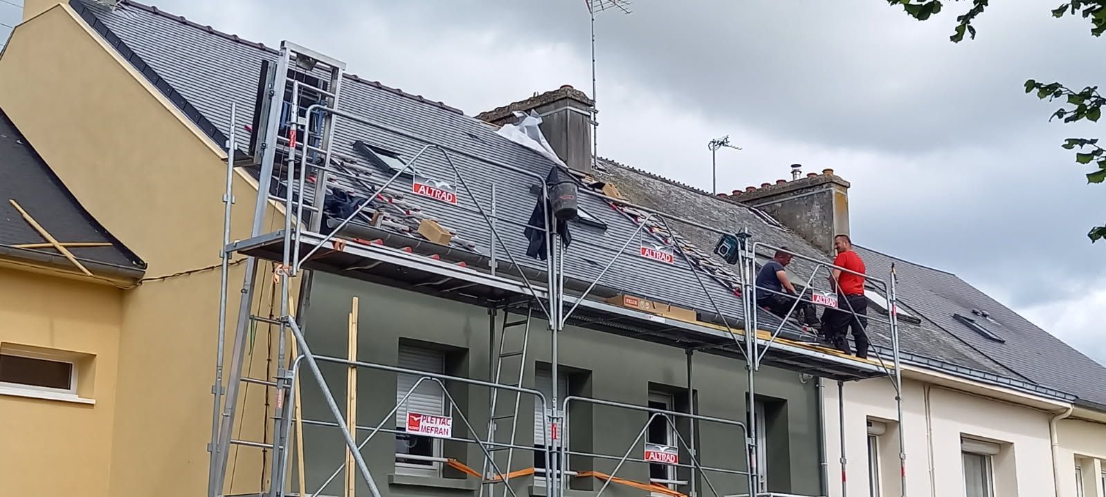 Couvreurs travaillant sur un toit avec des échafaudages. Maisons beiges et blanches, ciel gris.