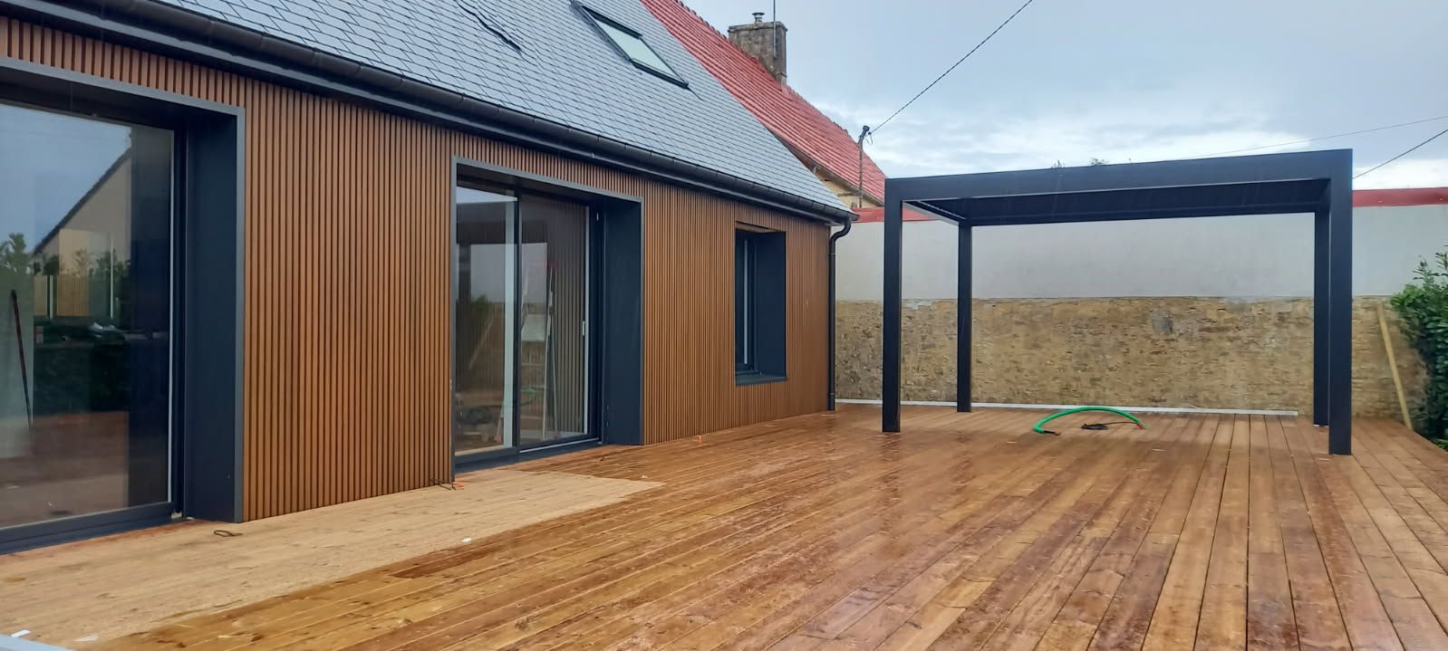 Maison en bois avec terrasse, pergola et ciel couvert.