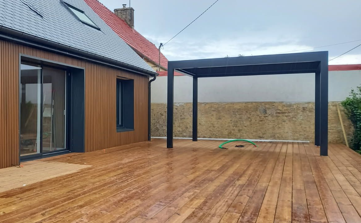 Terrasse en bois avec une pergola noire à côté d'une maison aux façades brunes.
