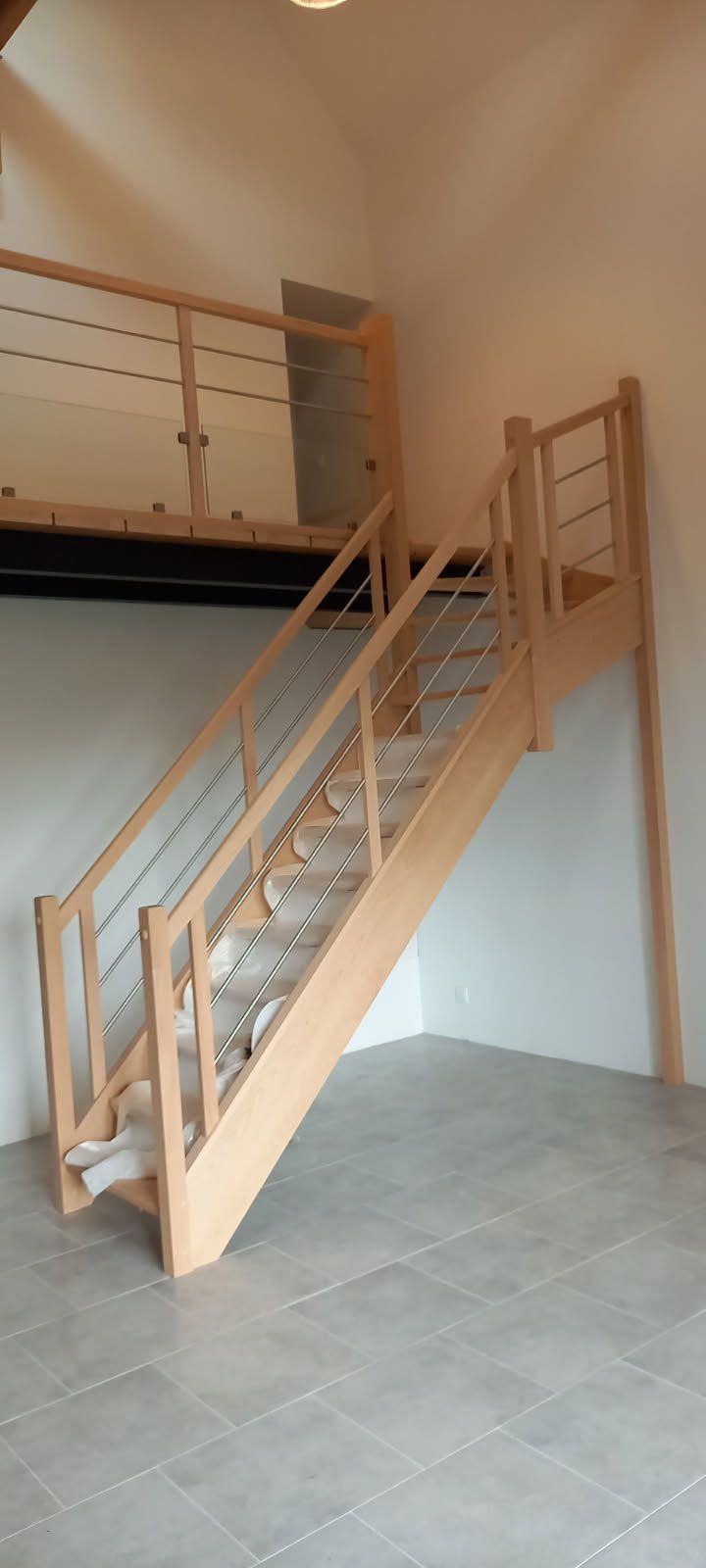 Escalier en bois avec rampe en métal dans une pièce lumineuse, menant à un deuxième niveau.