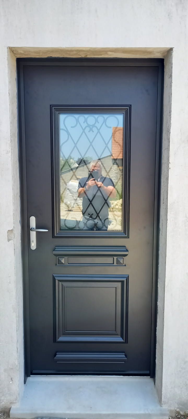 Porte extérieure noire avec fenêtre en verre, reflétant une personne prenant une photo.