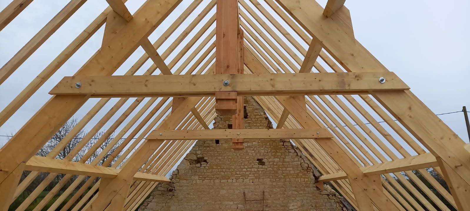Charpente en bois sur fond de ciel nuageux. Des poutres brunes forment la structure, soutenue par des supports verticaux.
