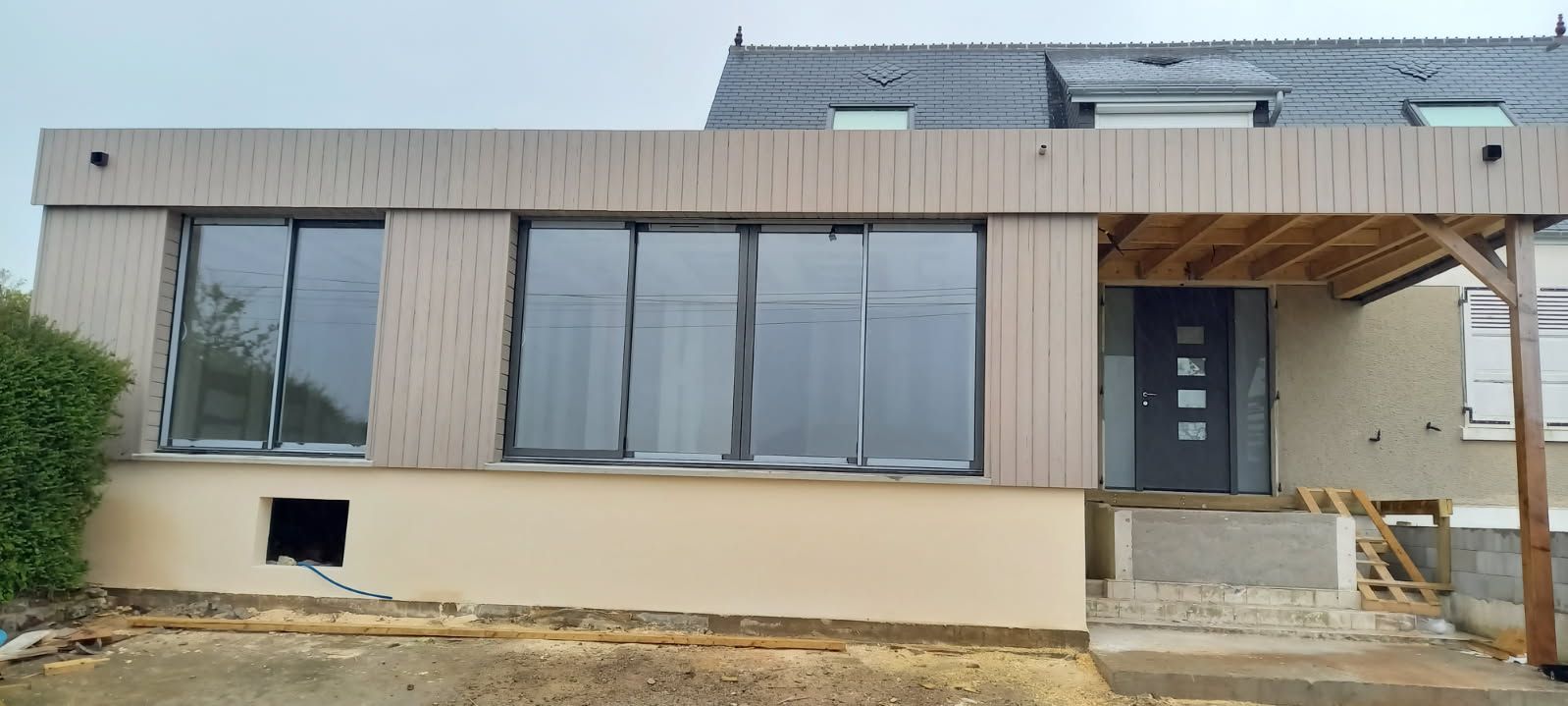 Extérieur d'un bâtiment avec une façade moderne, de grandes fenêtres et une entrée couverte en construction.