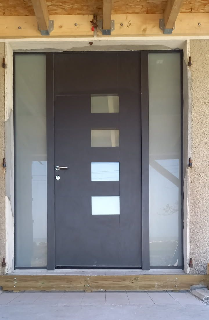 Porte d'entrée grise avec panneaux de verre, marches et extérieur en stuc texturé.