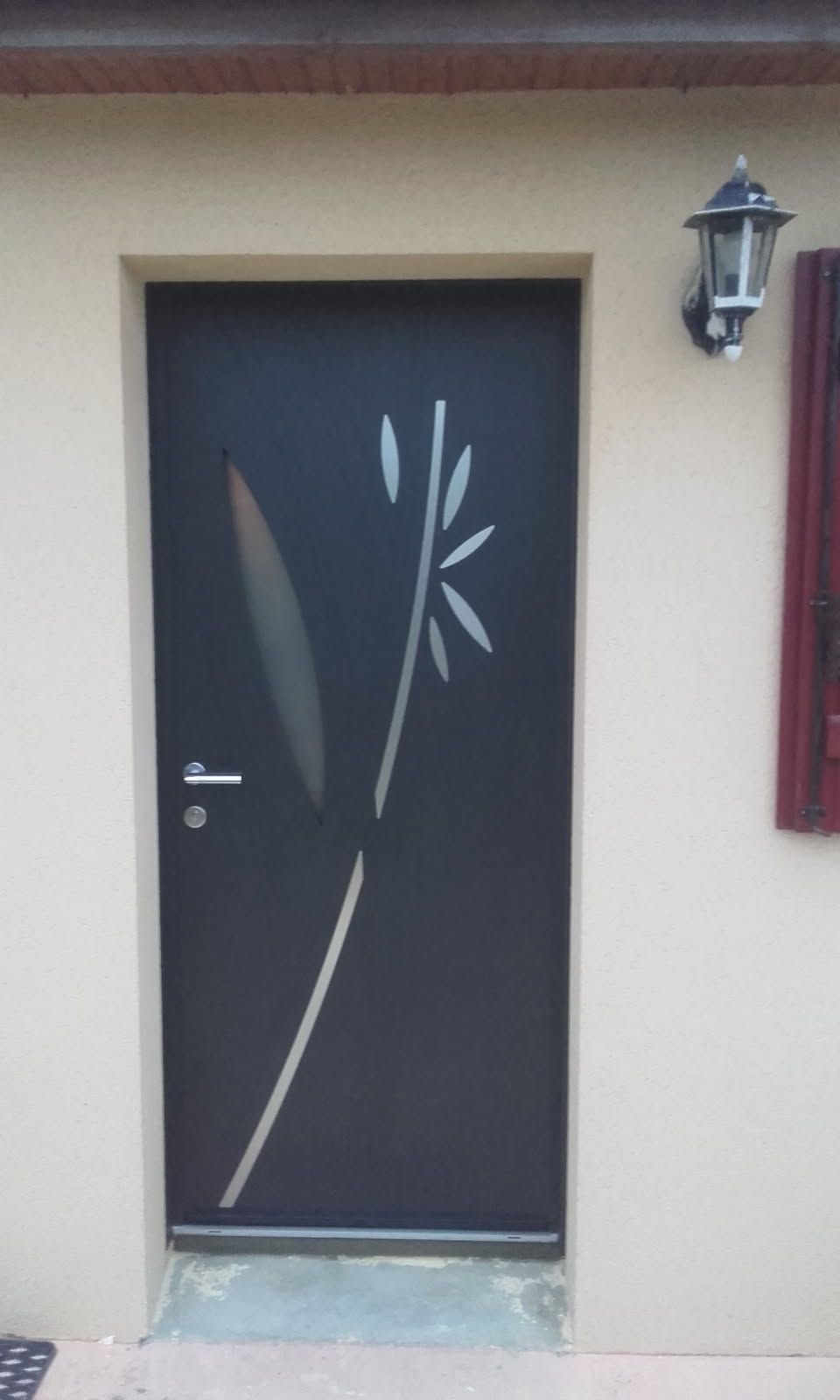 Porte noire avec motif de bambou gravé ; à côté d'un mur avec une applique.