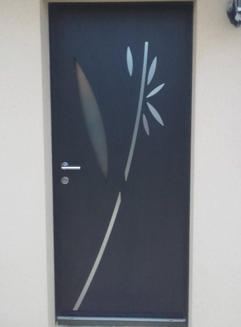 Porte noire avec motif floral gravé, encastrée dans un mur beige clair.