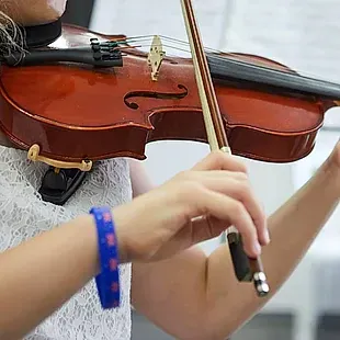 Una mujer toca un violín con una pulsera azul en la muñeca.
