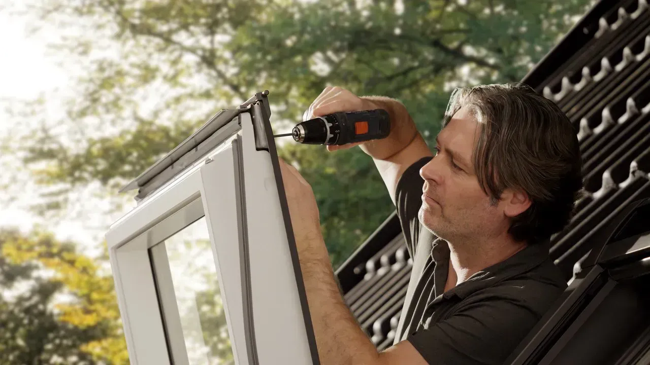 Un hombre está usando un taladro para arreglar una ventana.