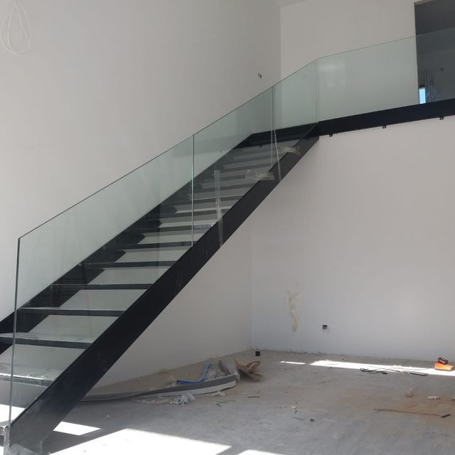 Una escalera negra con barandilla de cristal en una habitación vacía.