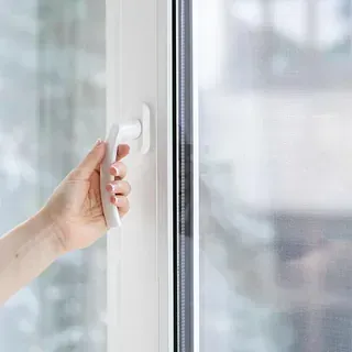 Una persona está abriendo una ventana con una manija blanca.