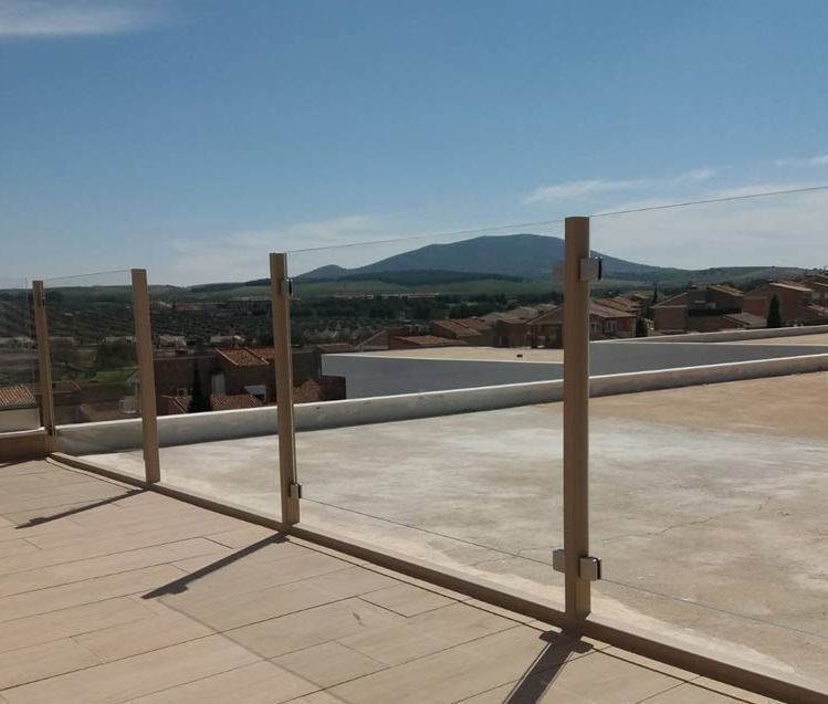 Un balcón con barandilla de cristal y una montaña al fondo.