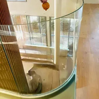 Una escalera con barandilla de vidrio curvado y piso de madera.