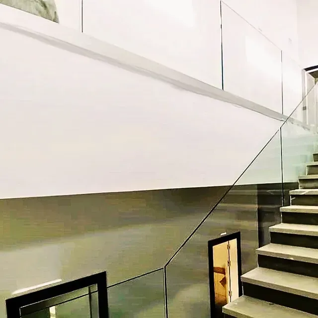 Una escalera con barandilla de cristal y una pared blanca.
