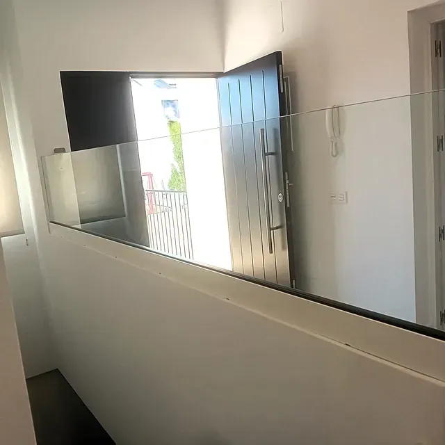 Una escalera con barandilla de cristal y una puerta al fondo.