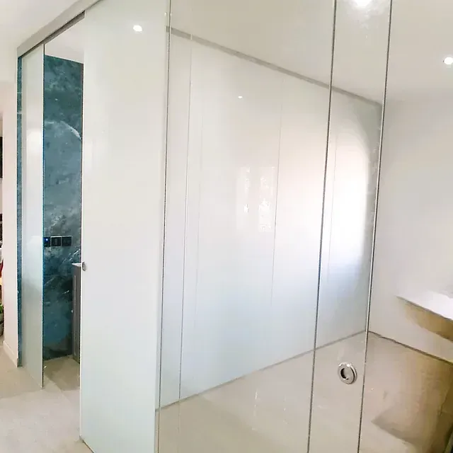 Un baño con paredes blancas y puertas de cristal.