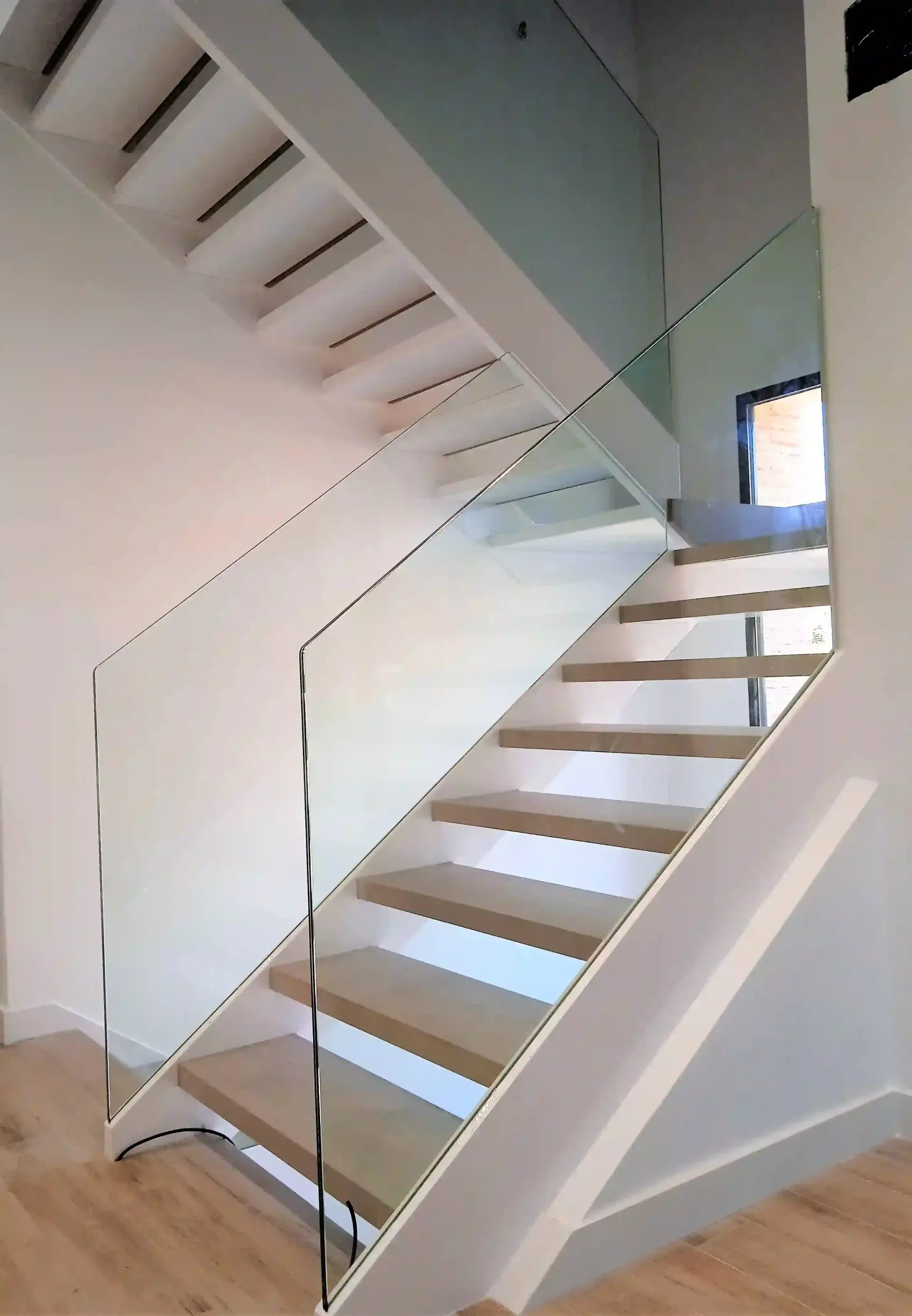 Una escalera con barandilla de cristal y escalones de madera.