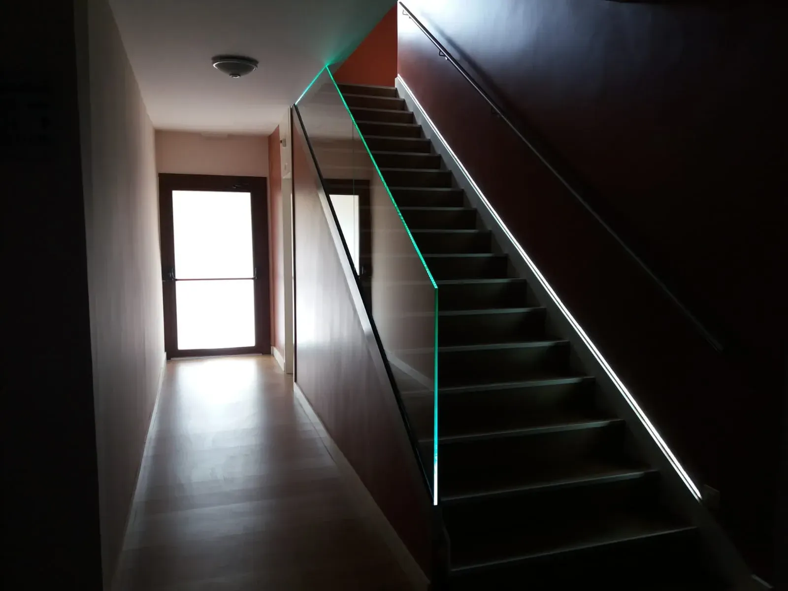 Un pasillo con escaleras y barandilla de cristal.