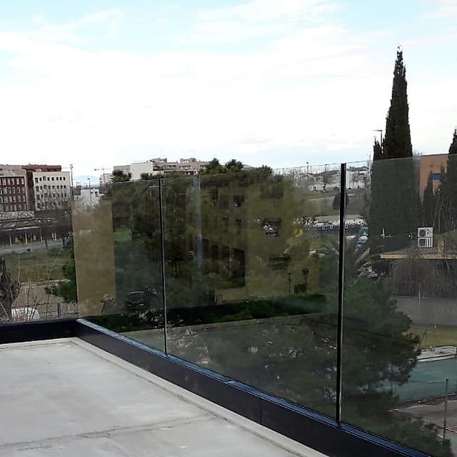 Un balcón con barandilla de cristal y vista a la ciudad.