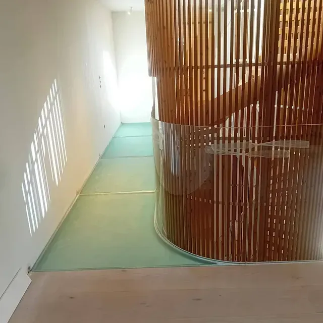 Una escalera de caracol de madera con barandilla de vidrio en un pasillo.