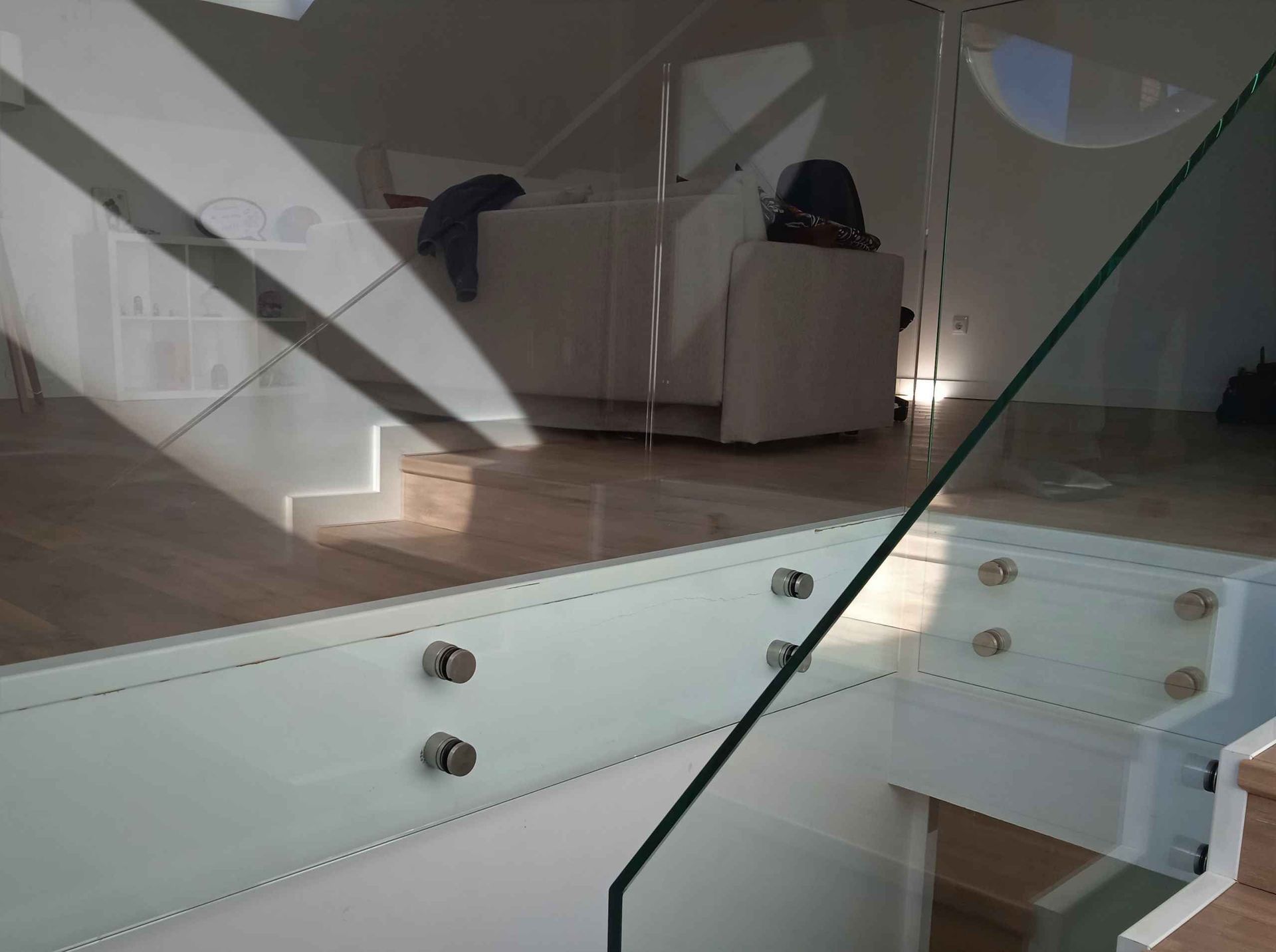 Una escalera con barandilla de cristal y un sofá al fondo.