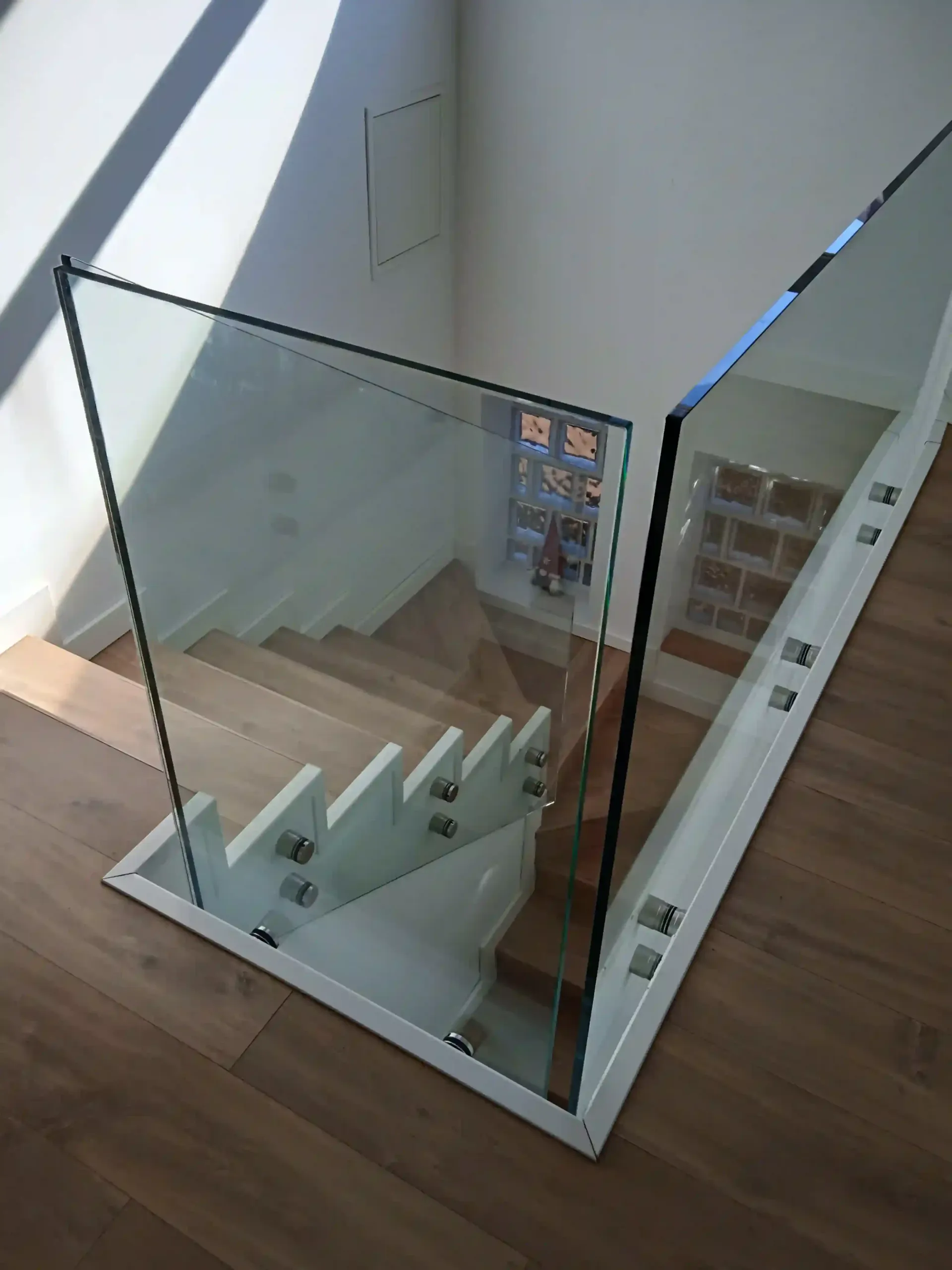 Una escalera con barandilla de cristal y escalones de madera.