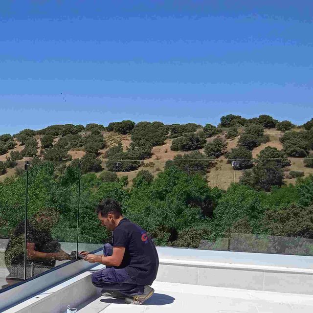 Un hombre está trabajando en una barandilla de vidrio en un balcón.