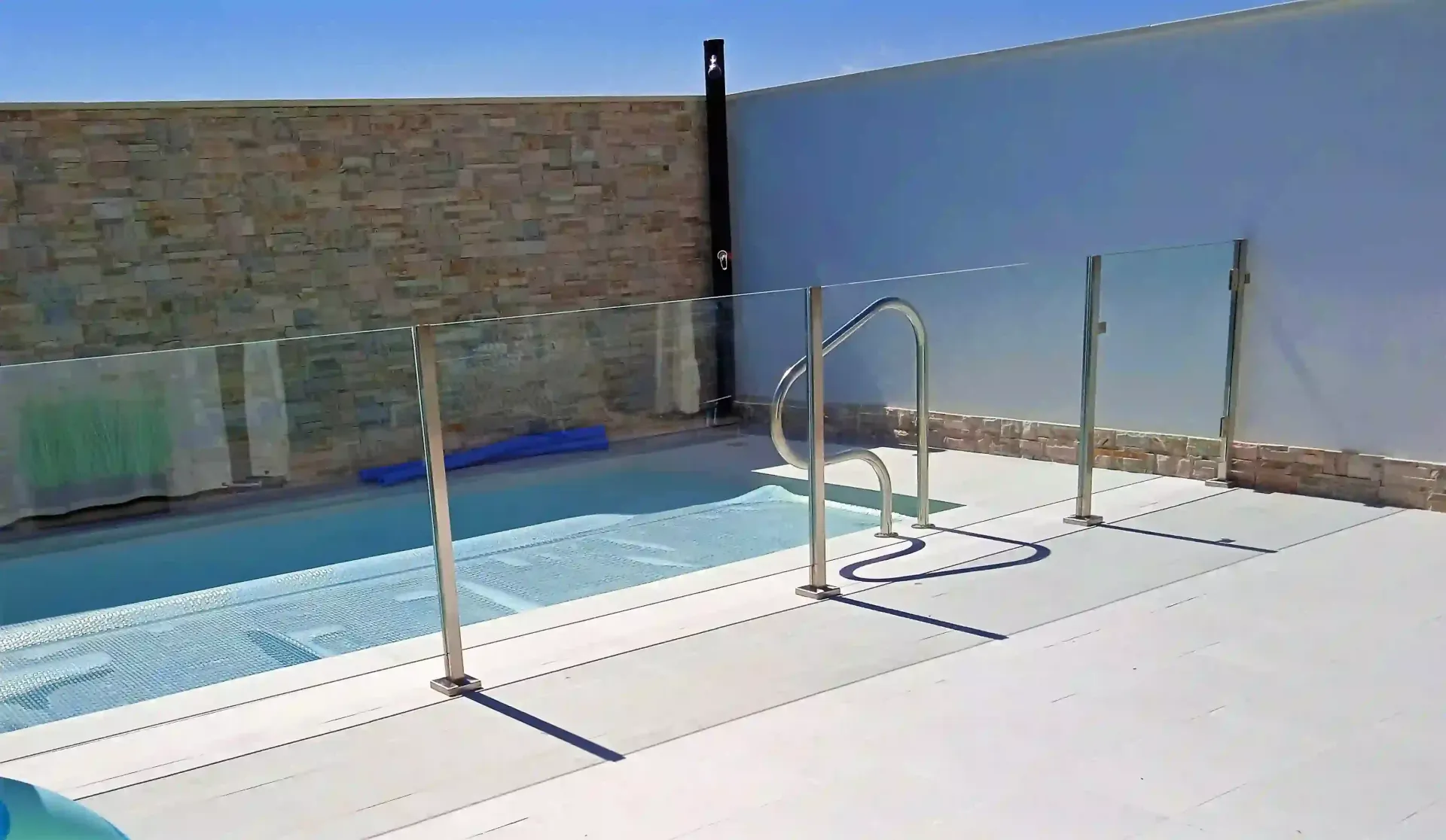 Una piscina con una valla de cristal y unas escaleras que conducen a ella.