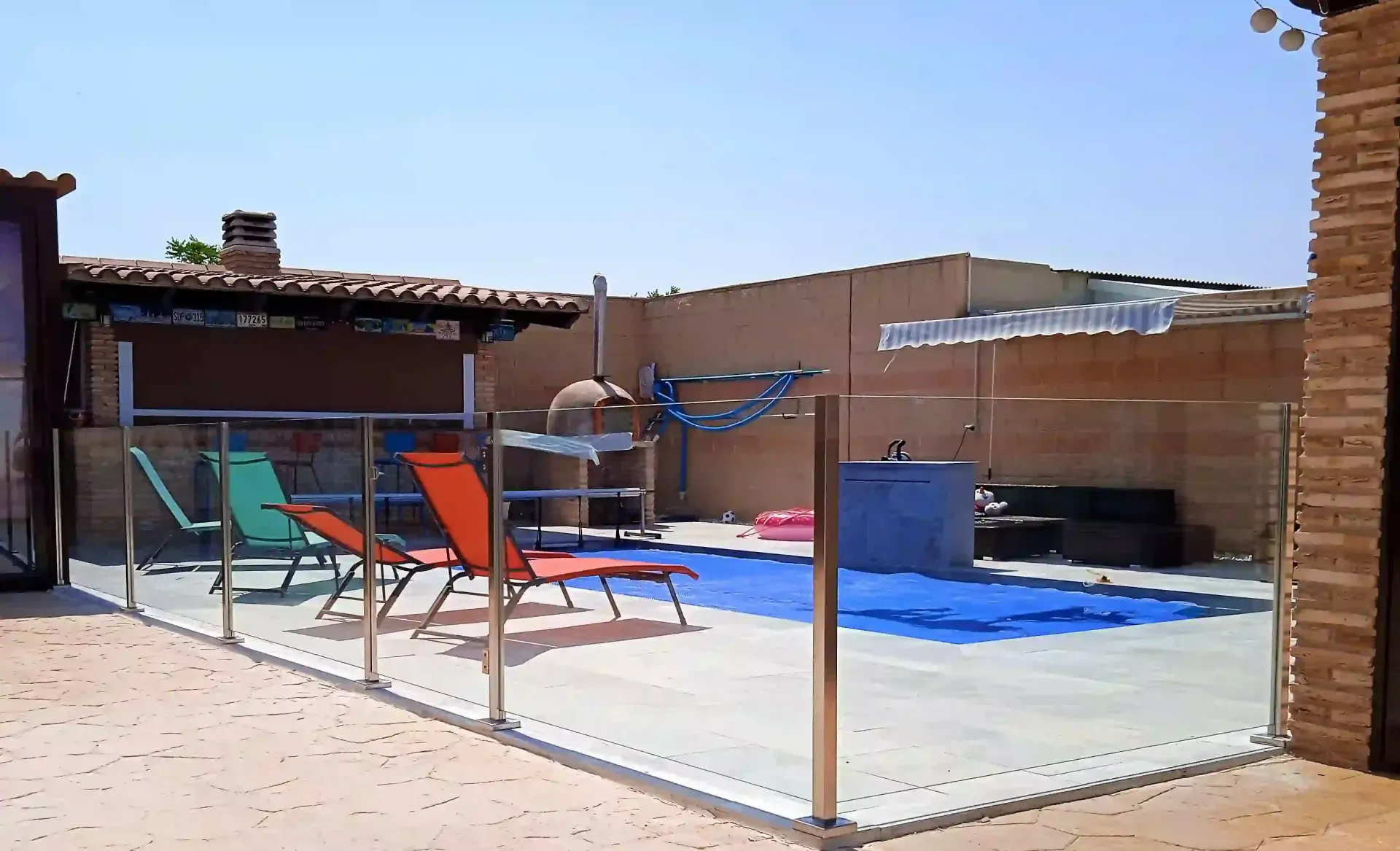 Una valla rodea una piscina con sillas y sombrillas.