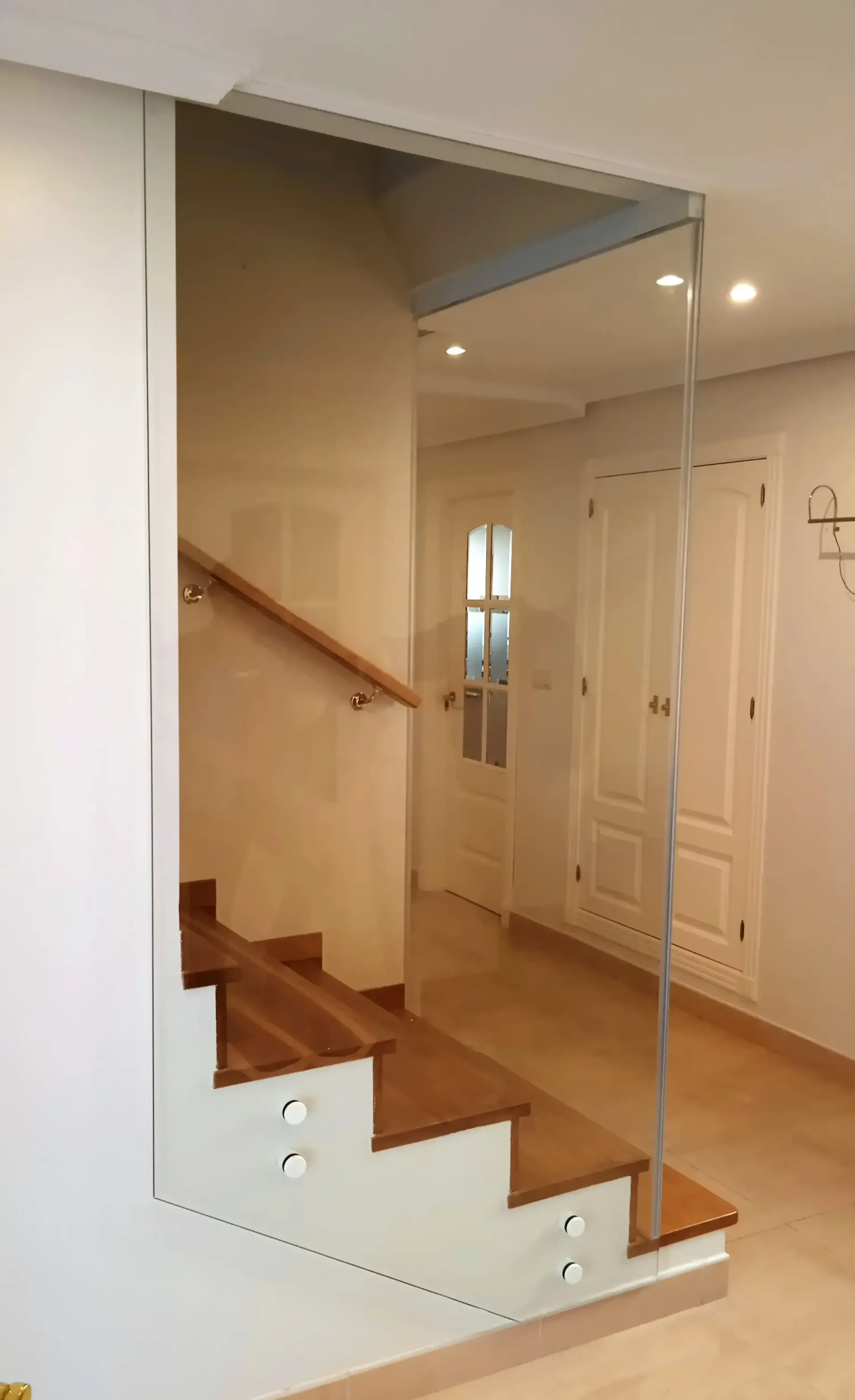 Una escalera de madera con barandilla de cristal en un pasillo.