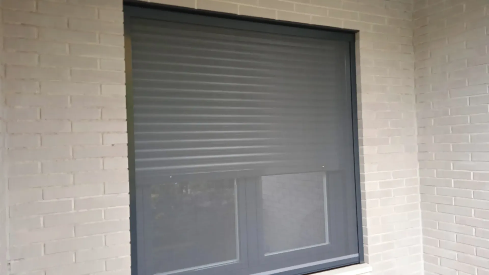 Una ventana con una mosquitera está en una pared de ladrillos.