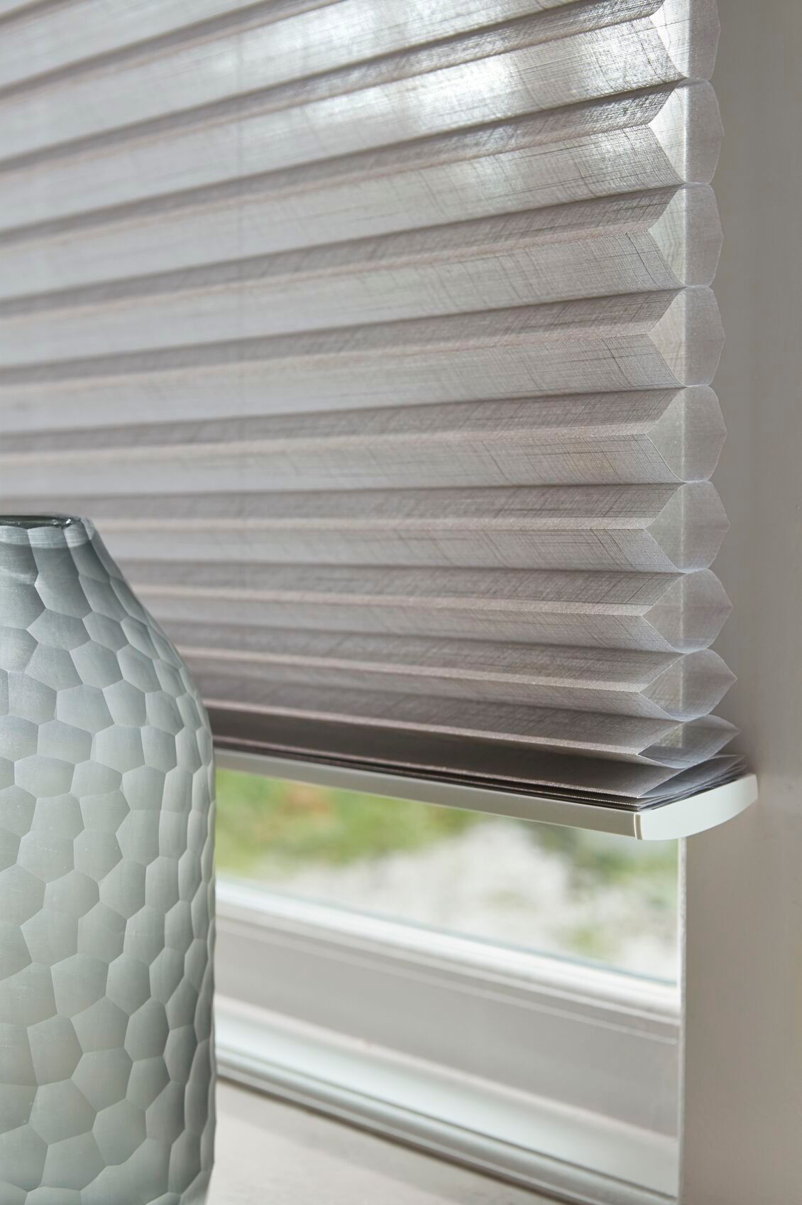 Un jarrón está colocado en el alféizar de una ventana, al lado de una persiana.