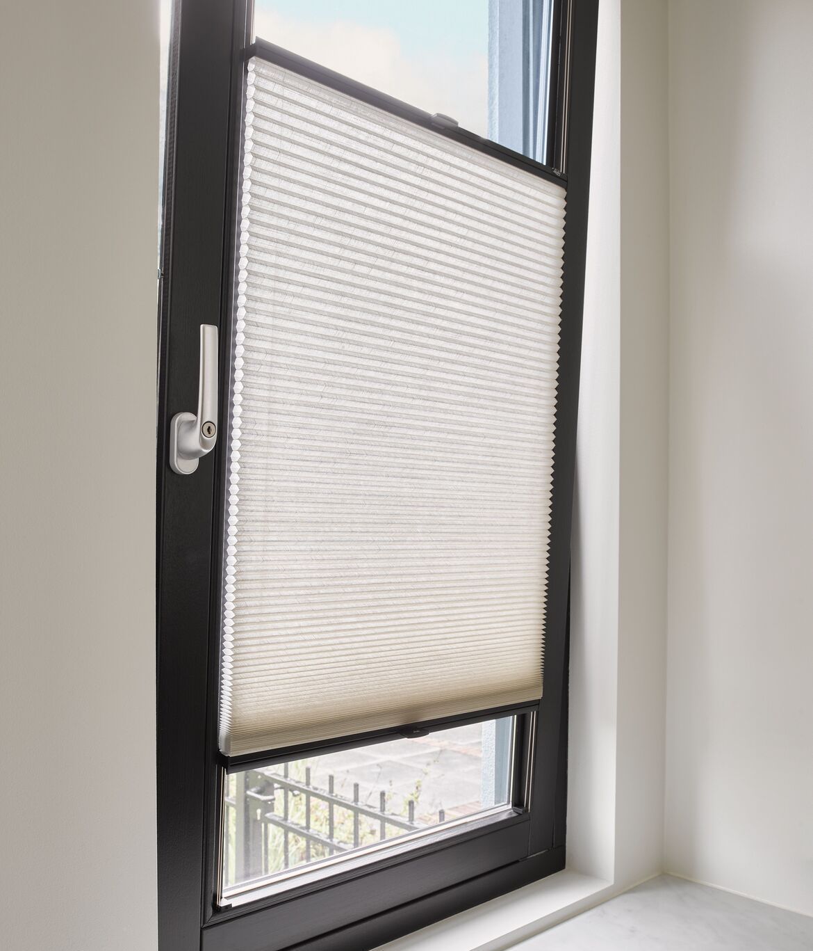 Una ventana con un marco negro y una persiana blanca.