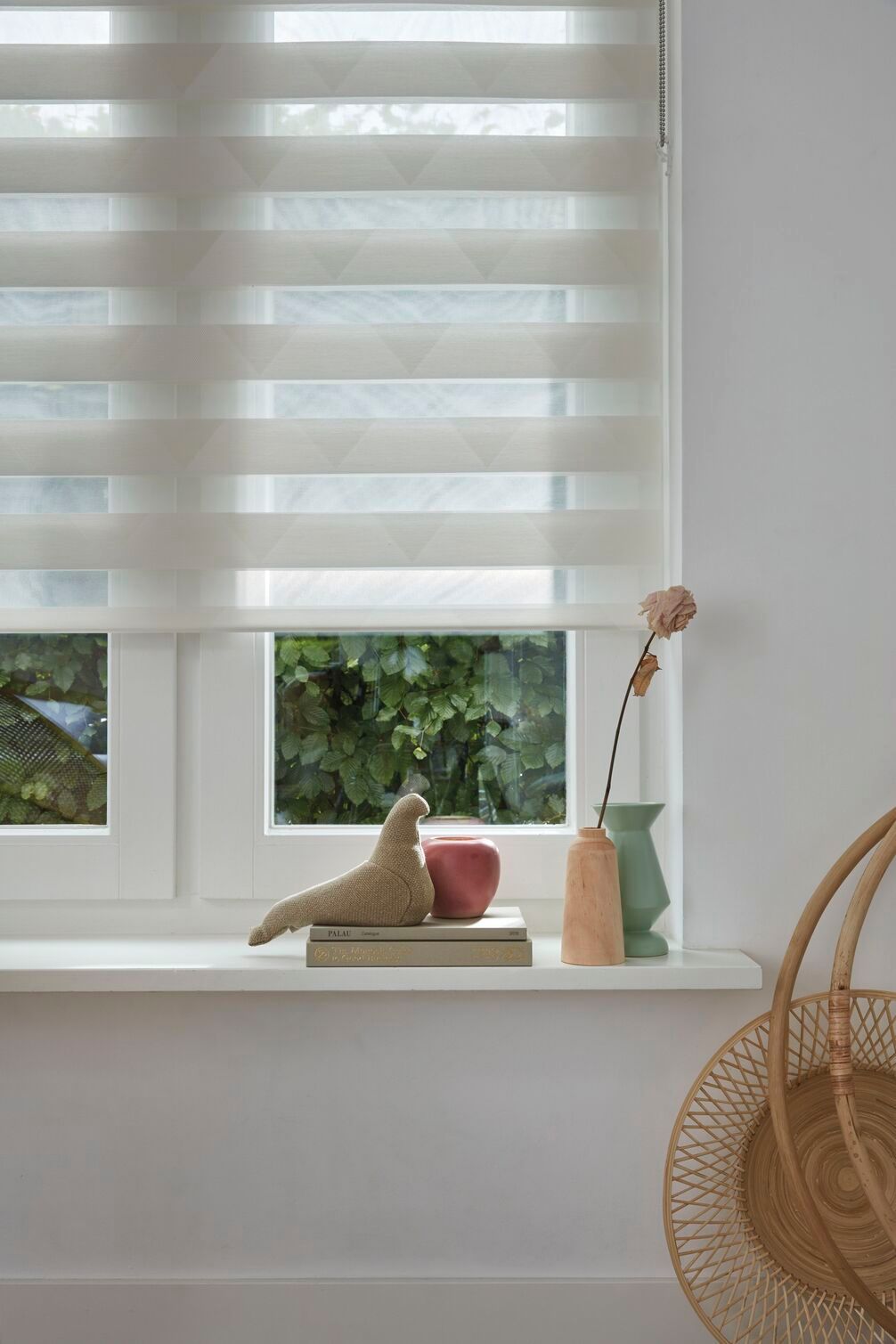 Una ventana con una persiana y un jarrón con flores en el alféizar.