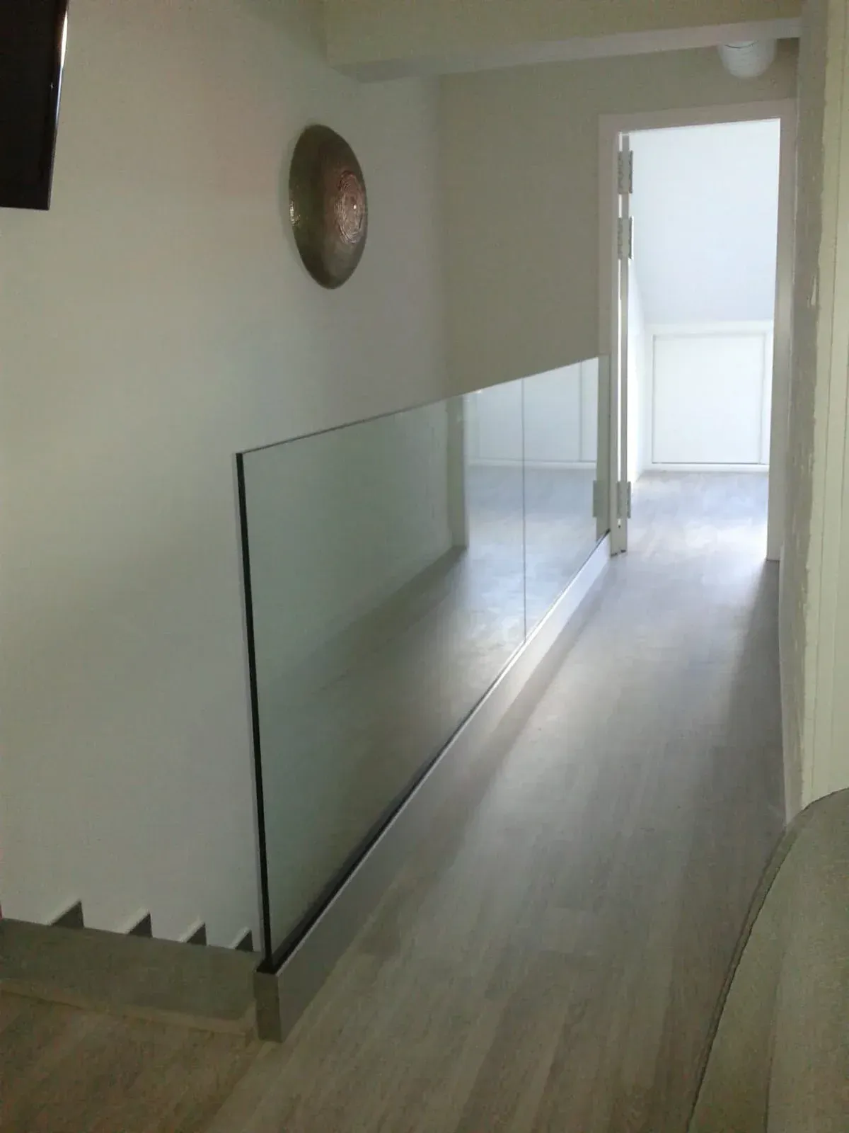 Un pasillo con escaleras y barandilla de cristal.