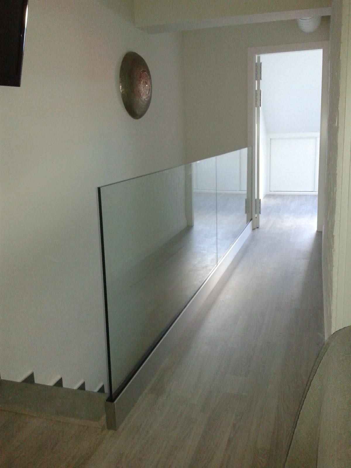 Un pasillo con escaleras y barandilla de cristal.