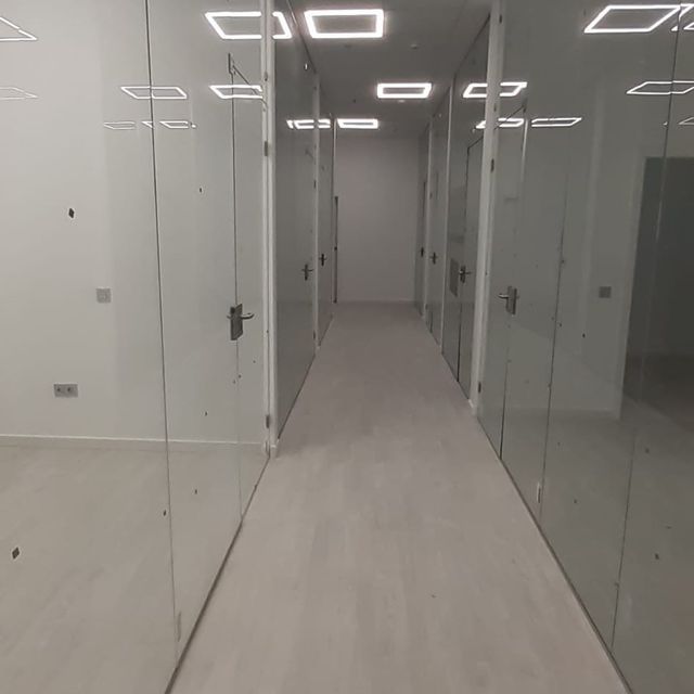 Un largo pasillo con paredes y puertas de vidrio en un edificio de oficinas.