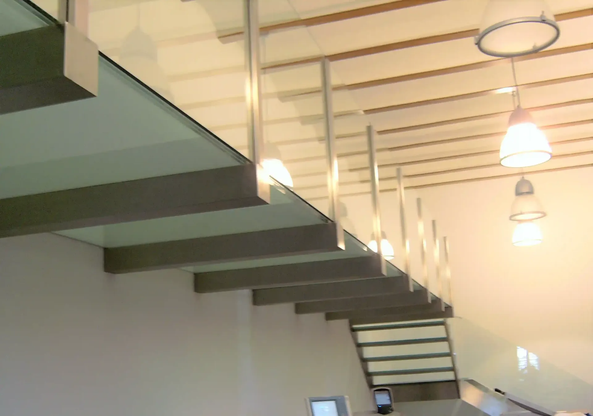 Una escalera con barandilla de cristal y luces colgando del techo.