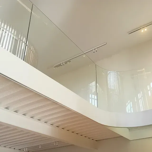 Una escalera con barandilla de cristal y techo blanco.