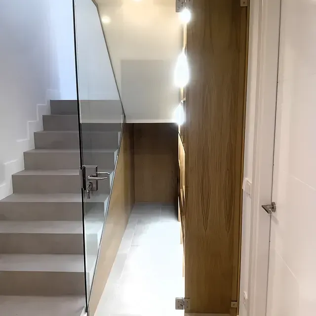 Un pasillo con escaleras y barandilla de cristal.