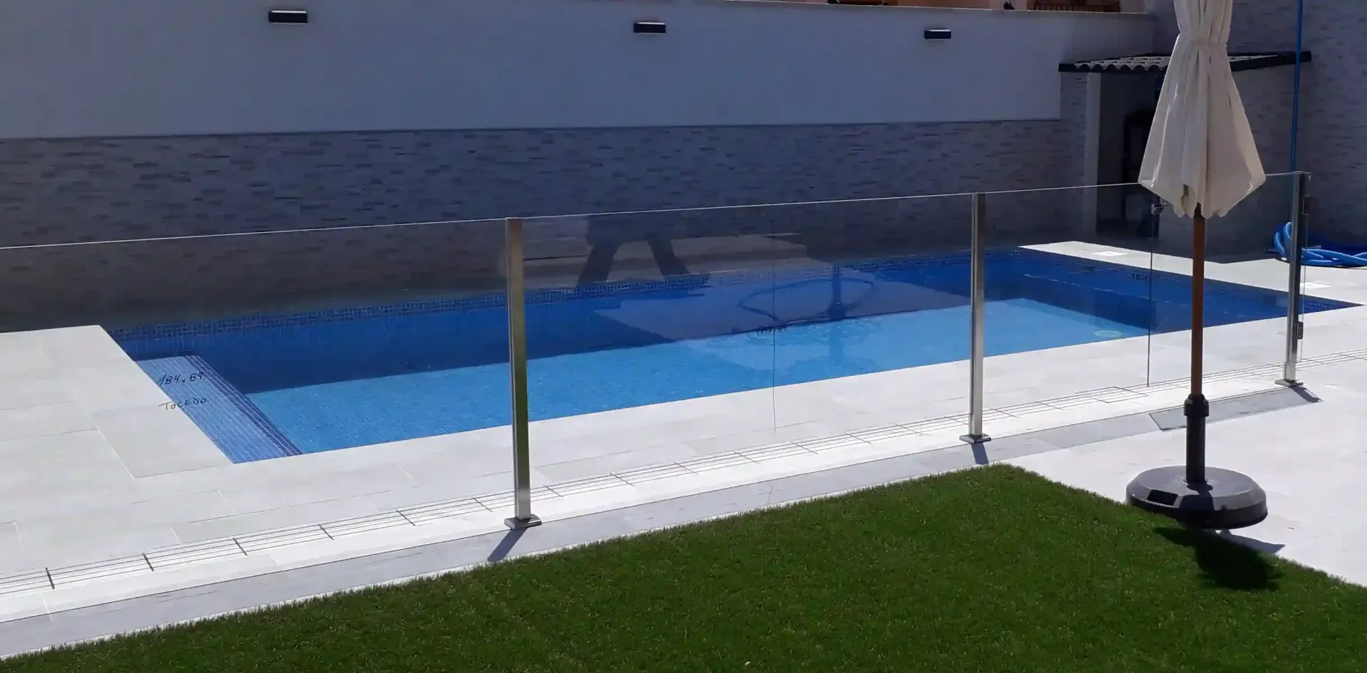 Una piscina con una valla de cristal y una sombrilla blanca