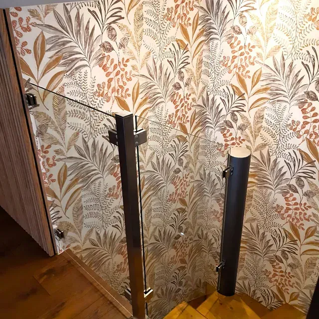 Una escalera con barandilla de cristal y papel pintado floral.