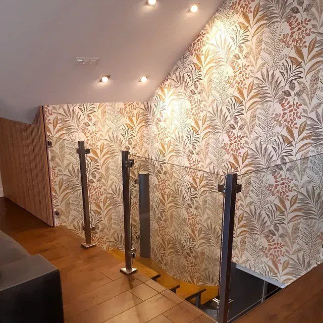 Una escalera con barandilla de cristal y papel pintado en la pared.