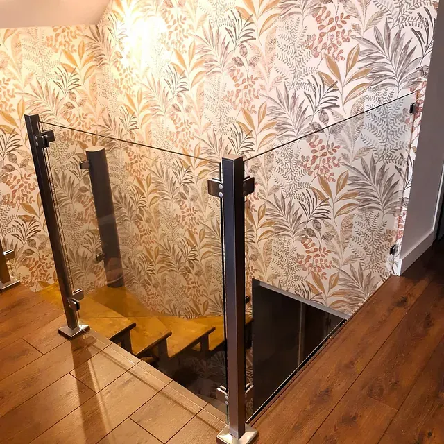 Una escalera con barandilla de cristal y un papel pintado floral en la pared.