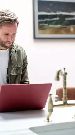 Un hombre está sentado en una mesa usando una computadora portátil.