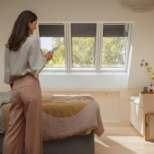 Una mujer está parada en un dormitorio al lado de una cama sosteniendo un control remoto.