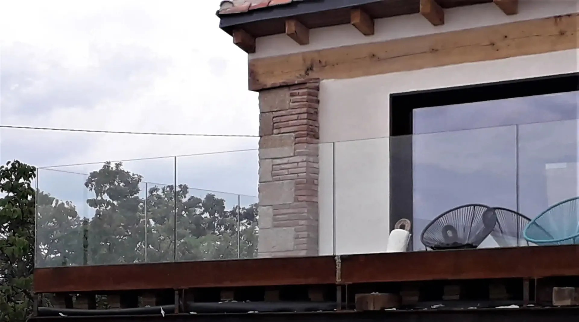 Un balcón con barandilla de vidrio en el costado de una casa.