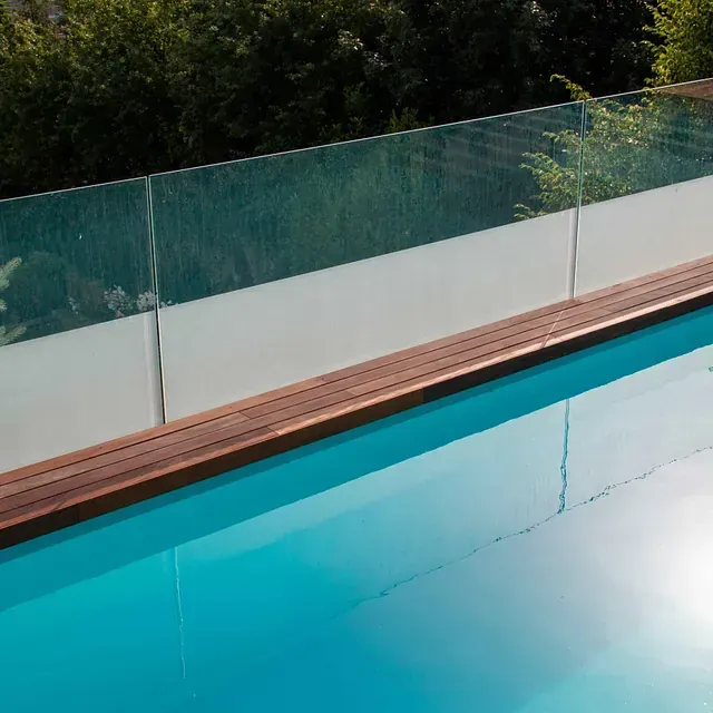 Una piscina con barandilla de cristal y terraza de madera